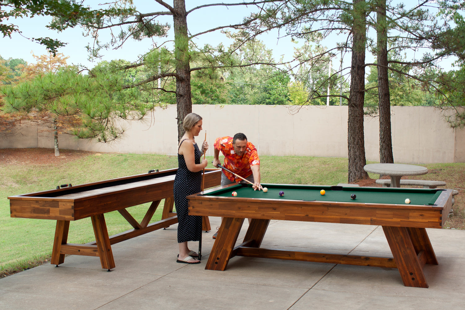 Legacy Billiards 8 Ft Barren Outdoor Pool Table in Natural Acacia Finish with People Playing Pool Outside and Emory Outdoor Shuffleboard