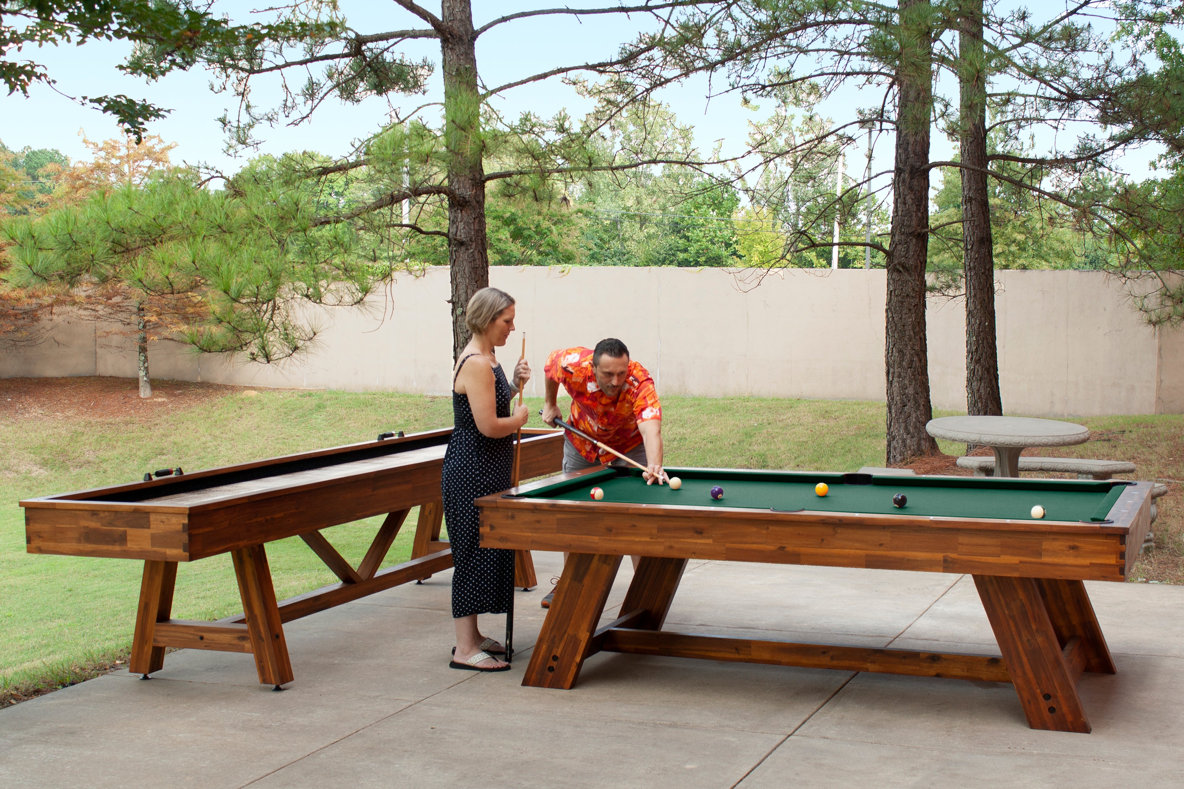Legacy Billiards 7 Ft Barren Outdoor Pool Table in Natural Acacia Finish with People Playing Pool Outside and Emory Outdoor Shuffleboard