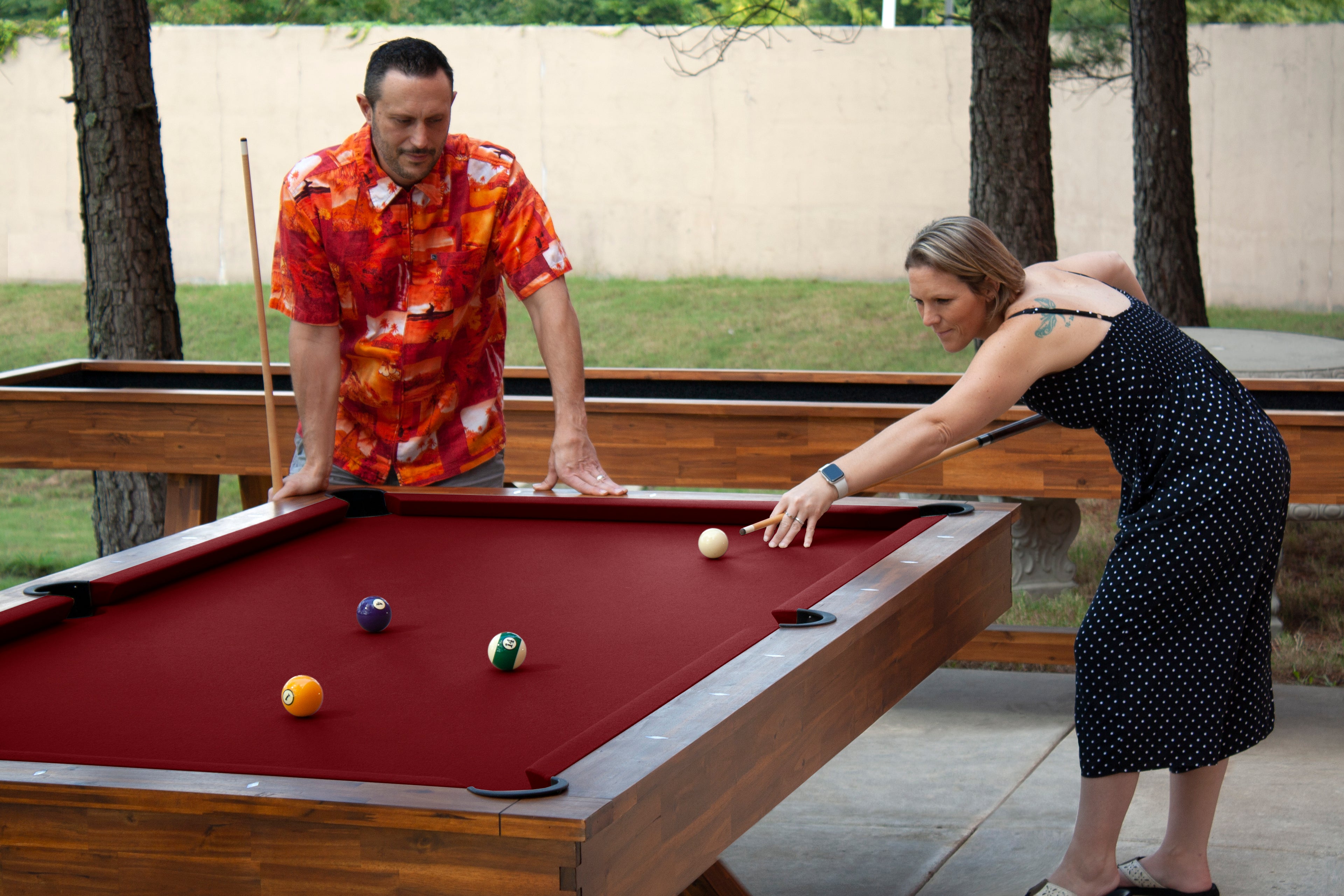 Legacy Billiards 7 Ft Cumberland Outdoor Pool Table in Natural Acacia Finish with People Playing Pool Outside and Emory Outdoor Shuffleboard
