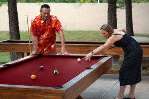 Legacy Billiards 8 Ft Cumberland Outdoor Pool Table in Natural Acacia Finish with People Playing Pool Outside and Emory Outdoor Shuffleboard